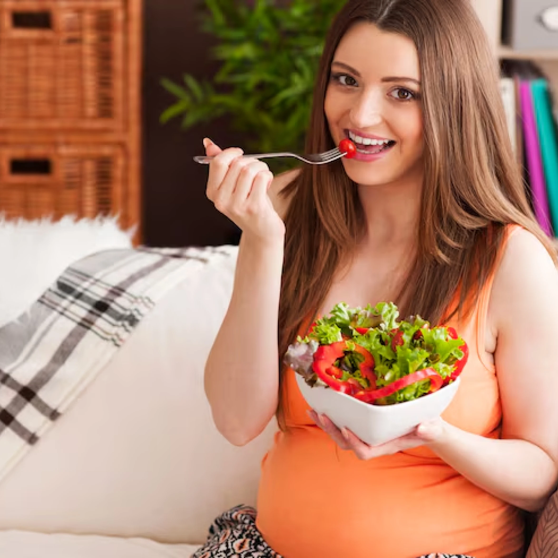 A smiling pregnant woman eating a fresh salad at home